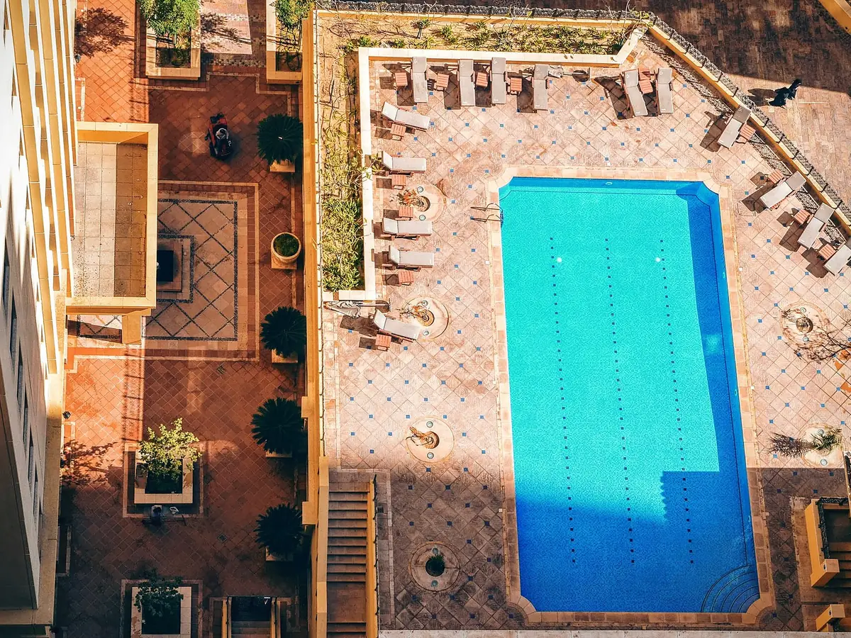 Pool deck with a patterned finish and lounge chairs around a rectangular pool, seen from above